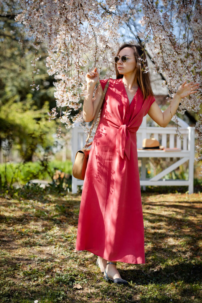 A beautiful young woman walk through a meadow in a blooming spring garden against the backdrop of a white elegant blossom sakura, an exquisite bench