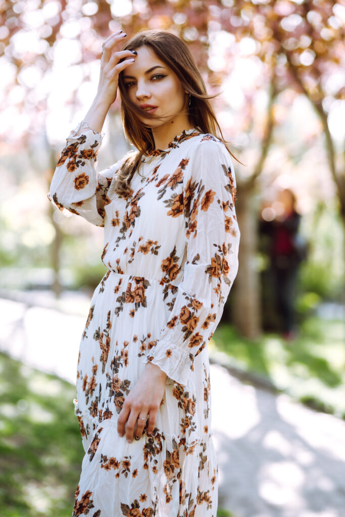 Beautiful young woman near the blooming spring tree. Attractive girl enjoying her time outside in park.