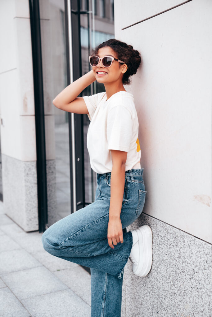 Young beautiful smiling hipster woman in trendy summer white t-shirt and jeans clothes. Carefree woman, posing in the street at sunny day. Positive model outdoors. Cheerful and happy