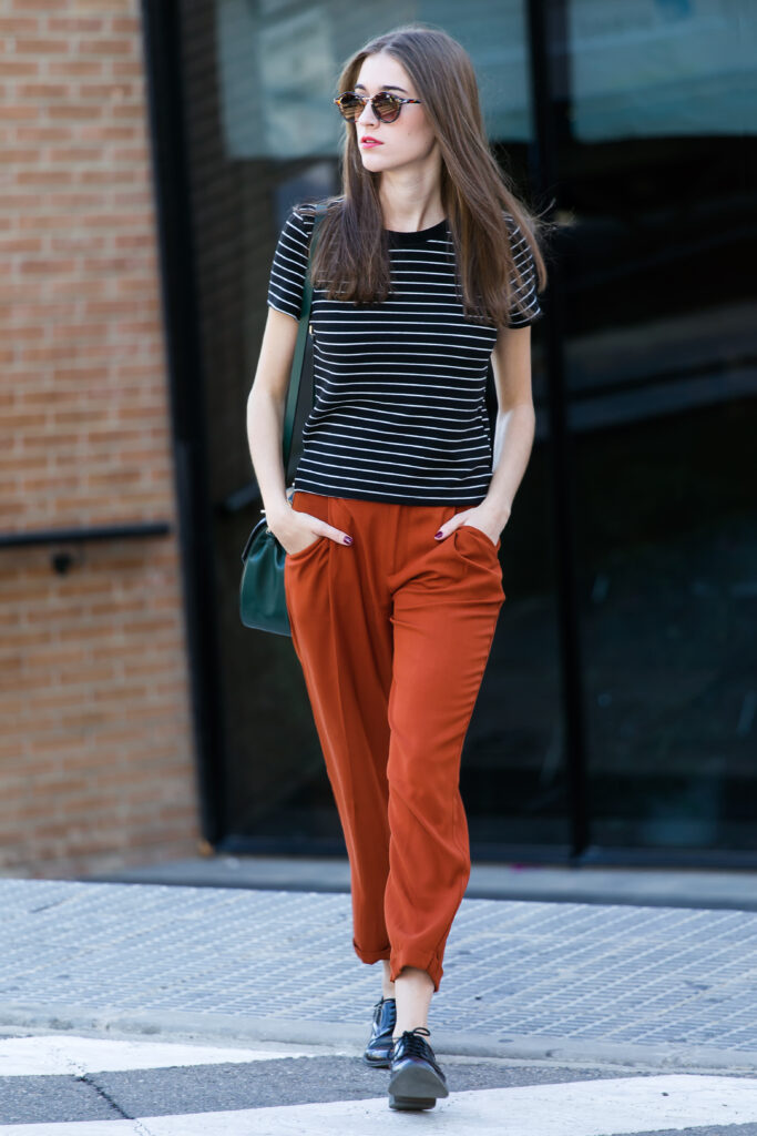 Front view of a beautiful young woman looking away with her hands in her pockets posing on the street in fashionable clothes while crossing a pedestrian crossing