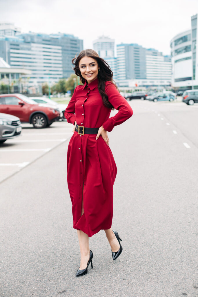 Handsome younng caucasian female with pretty face in a beautiful red dress with a length below the knee walks to the street